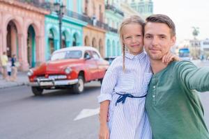 familj av pappa och liten flicka tar selfie i populär område i gammal Havanna, kuba. liten unge och ung far utomhus på en gata av havana foto