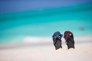 sommar svart flip flops med solglasögon på vit strand foto