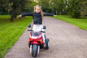 förtjusande liten flicka har roligt på henne leksak motorcykel foto