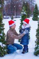 Lycklig familj i santa hattar med jul träd utomhus- foto