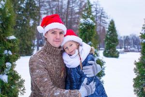 Lycklig familj i santa hattar med jul träd utomhus- foto