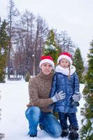 Lycklig far och unge i santa hattar med jul träd utomhus- foto