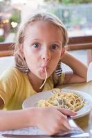 förtjusande liten flicka äter spaghetti i utomhus restaraunt foto