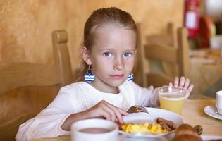 förtjusande liten flicka har frukost på inomhus- Kafé foto