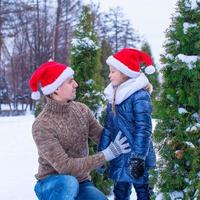 Lycklig far och liten flicka i santa hattar med jul träd utomhus- foto