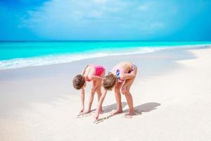 Lycklig liten flickor spela med sand på de strand. två barn framställning sand slott med vit sand foto