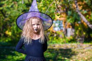 förtjusande liten flicka i häxa kostym kastar en stava på halloween foto