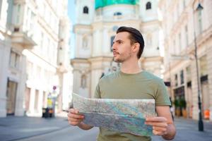 man turist med en stad Karta och ryggsäck i Europa gata. caucasian pojke ser med Karta av europeisk stad. foto