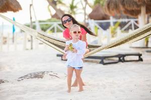 mor med henne bebis dotter i hängmatta på en perfekt vit sand strand foto