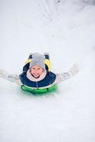 förtjusande liten Lycklig flicka sledding i vinter- snöig dag. foto