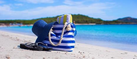 blå väska, sugrör hatt, flip flops och handduk på vit tropisk strand foto