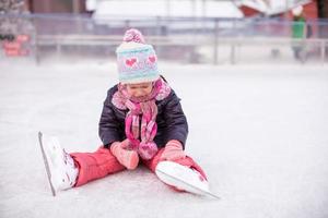 liten ledsen flicka Sammanträde på skridskoåkning rink efter de falla foto