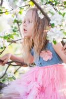 porträtt av skön liten flicka i blomning äpple träd trädgård på vår dag foto