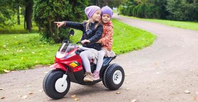 Lycklig liten söt flickor rida en motorcykel utanför foto