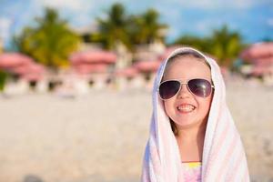 förtjusande liten flicka i solglasögon täckt med handduk på tropisk strand foto