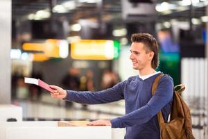ung man med pass och ombordstigning biljetter på de främre skrivbord i flygplats foto