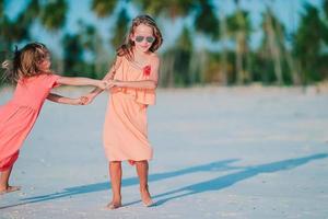 liten Lycklig rolig flickor ha en massa av roligt på tropisk strand spelar tillsammans. foto