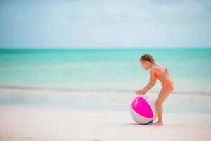 liten förtjusande flicka spelar på vit strand med luft boll foto