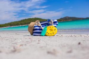 rand väska, sugrör hatt, solkräm och frisbee på vit sandig tropisk strand foto