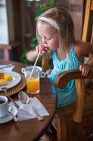 förtjusande liten flicka har frukost och dricka frukt cocktail foto