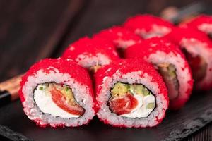 kalifornien sushi rulla med lax, avokado gurka och tobiko kaviar eras på svart styrelse närbild - japansk mat foto