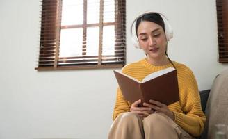 leende flicka avkopplande på Hem, hon är spelar musik använder sig av en smartphone och bär vit hörlurar foto