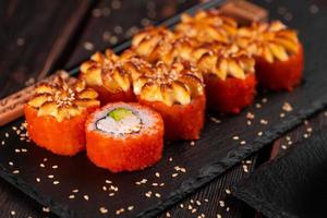 kalifornien sushi rulla med krabba, avokado och tobiko kaviar eras på svart styrelse närbild - japansk asiatisk mat foto