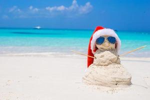 sandig snögubbe med röd santa hatt på vit karibiska strand foto