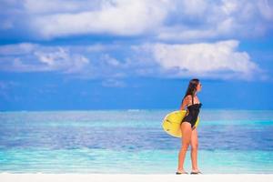 Lycklig smal surfa kvinna på vit strand med gul surfingbräda foto