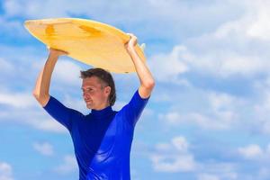 Lycklig ung surfa man på vit strand med gul surfingbräda foto