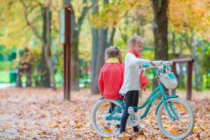 Lycklig liten flickor ridning en cykel på skön höst dag utomhus foto