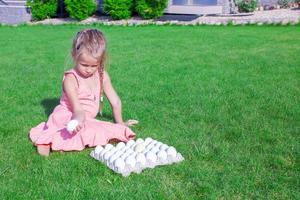 förtjusande liten flicka innehav en vit påsk ägg i henne gård foto