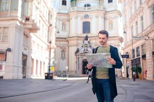 man turist med en stad Karta och ryggsäck i Europa gata. caucasian pojke ser med Karta av europeisk stad. foto