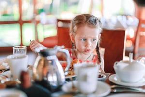 förtjusande liten flicka har frukost i Kafé foto