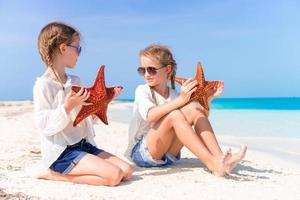 förtjusande liten flickor med sjöstjärnor på vit tömma strand foto