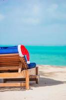 santa claus hatt på strand vilstol med turkos hav vatten och vit sand. jul semester begrepp foto