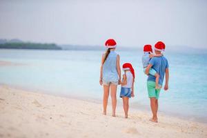 Lycklig skön familj i röd santa hattar på tropisk strand fira jul foto