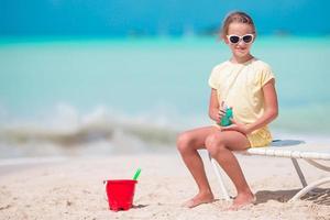 skön unge med flaska av Sol grädde på tropisk strand foto