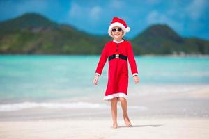 bedårande liten flicka i santa hatt på tropisk strand foto
