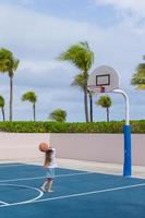 liten flicka med basketboll på domstol på tropisk tillflykt foto