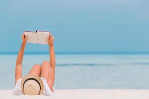 ung kvinna läsning bok under tropisk vit strand foto
