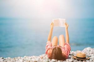 ung kvinna läsning bok under tropisk vit strand foto