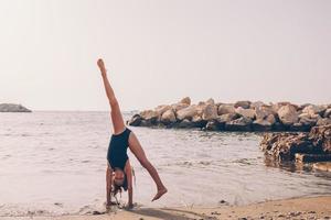 aktiva liten flicka på strand har en massa av roligt. söt unge framställning sportig övningar på de havsstrand foto