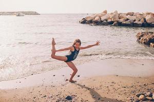 aktiva liten flicka på strand har en massa av roligt. söt unge framställning sportig övningar på de havsstrand foto