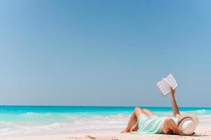 ung kvinna läsning bok på schäslong på de strand foto