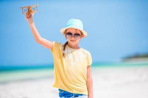 Lycklig liten flicka med leksak flygplan i händer på vit strand foto