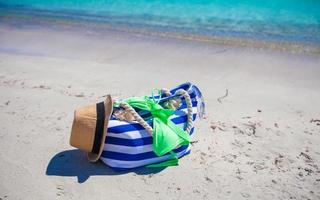 rand väska, sugrör hatt, solkräm och handduk på vit tropisk strand foto