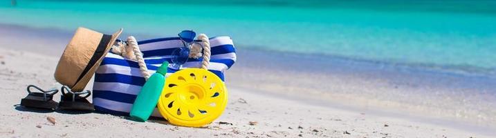 rand väska, sugrör hatt, solkräm och handduk på strand foto