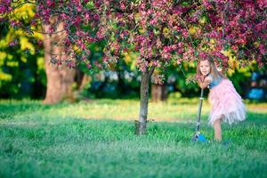 liten flicka har roligt på skoter i blomning äpple träd trädgård på vår dag foto