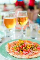 pizza med mozzarella ost, oliv, färsk tomat och pesto sås. eras på restaurang tabell med två öl foto